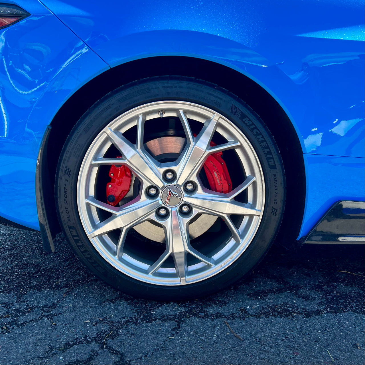 Close-up of a blue car wheel with silver rim and red brake calipers on a dark surface.