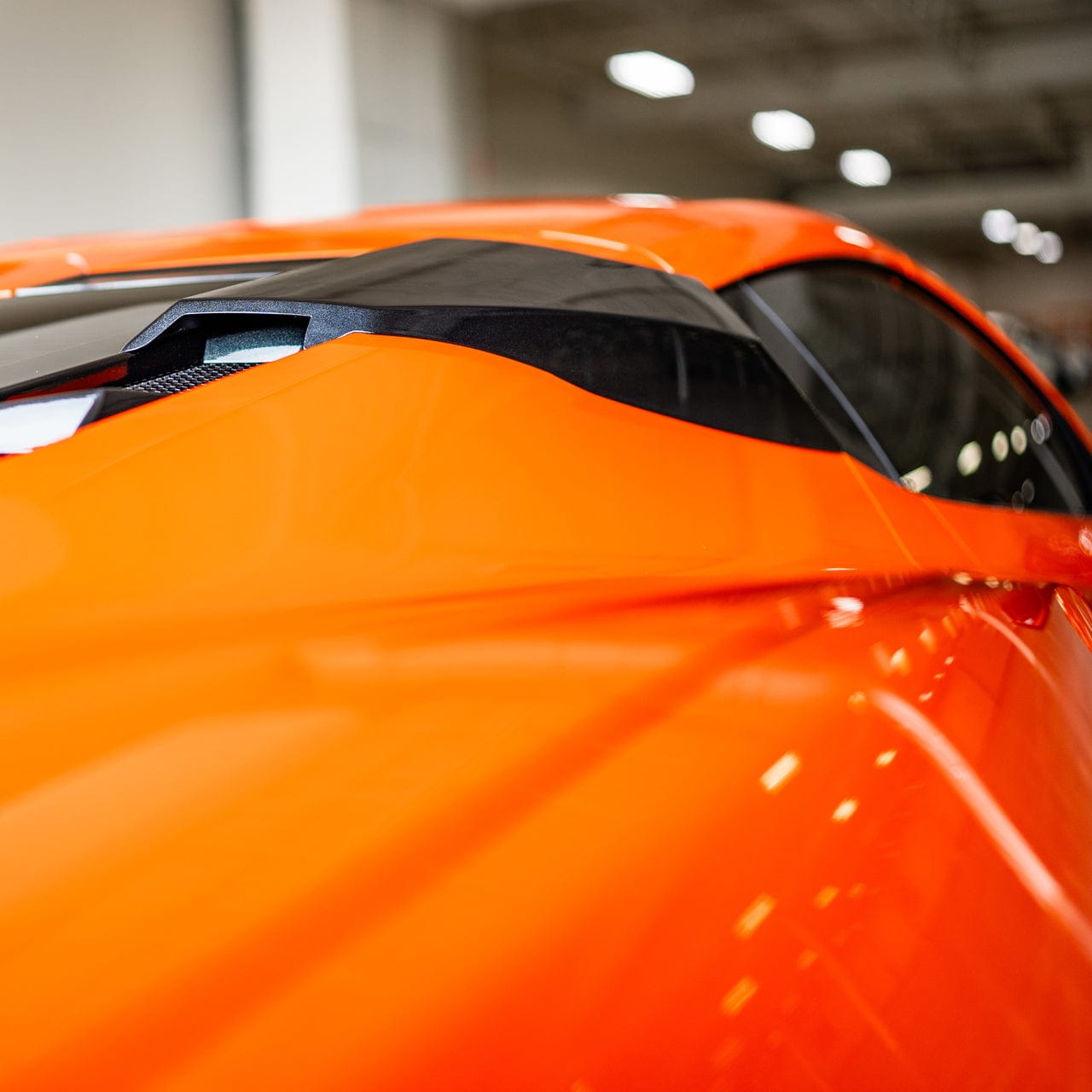 A rear view shot of a Carbon Flash Metallic Black ACS C8 RQ Intake Port installed on a Sebring Orange Corvette